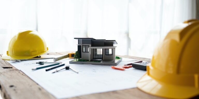 architectural model of houses on desk with drawing technical tools safty helmet and blueprint rolls