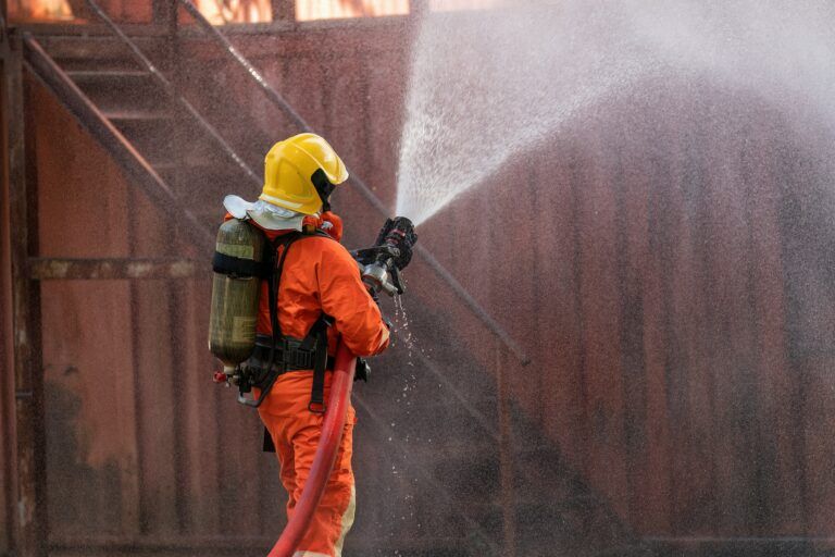 Fireman wearing fire protection suite and oxygen tank exercise hold hose spray water near fire truck